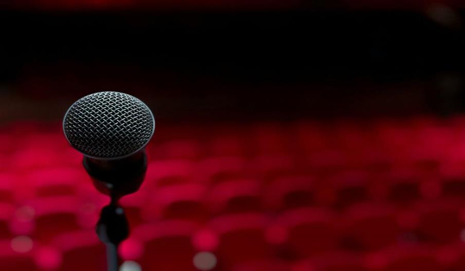 A microphone on a stage in front of red theatre seating
