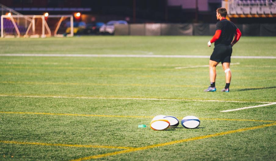 Four rugby balls on the ground with a player in the background